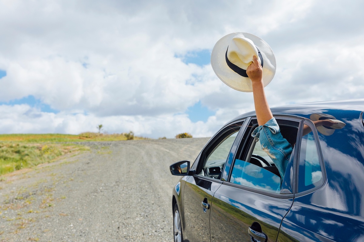 Photo of a car driving down the road on a sunny day, holding a hat out the window.